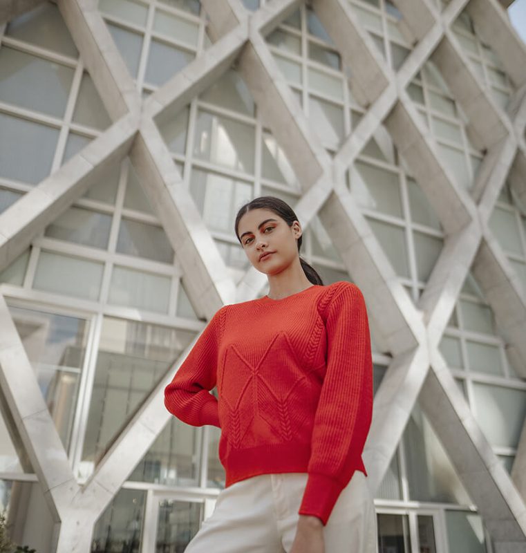 femme en pull rouge devant bâtiment La Défense Paris